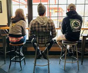 3 folks sitting at the rail in a restaurant